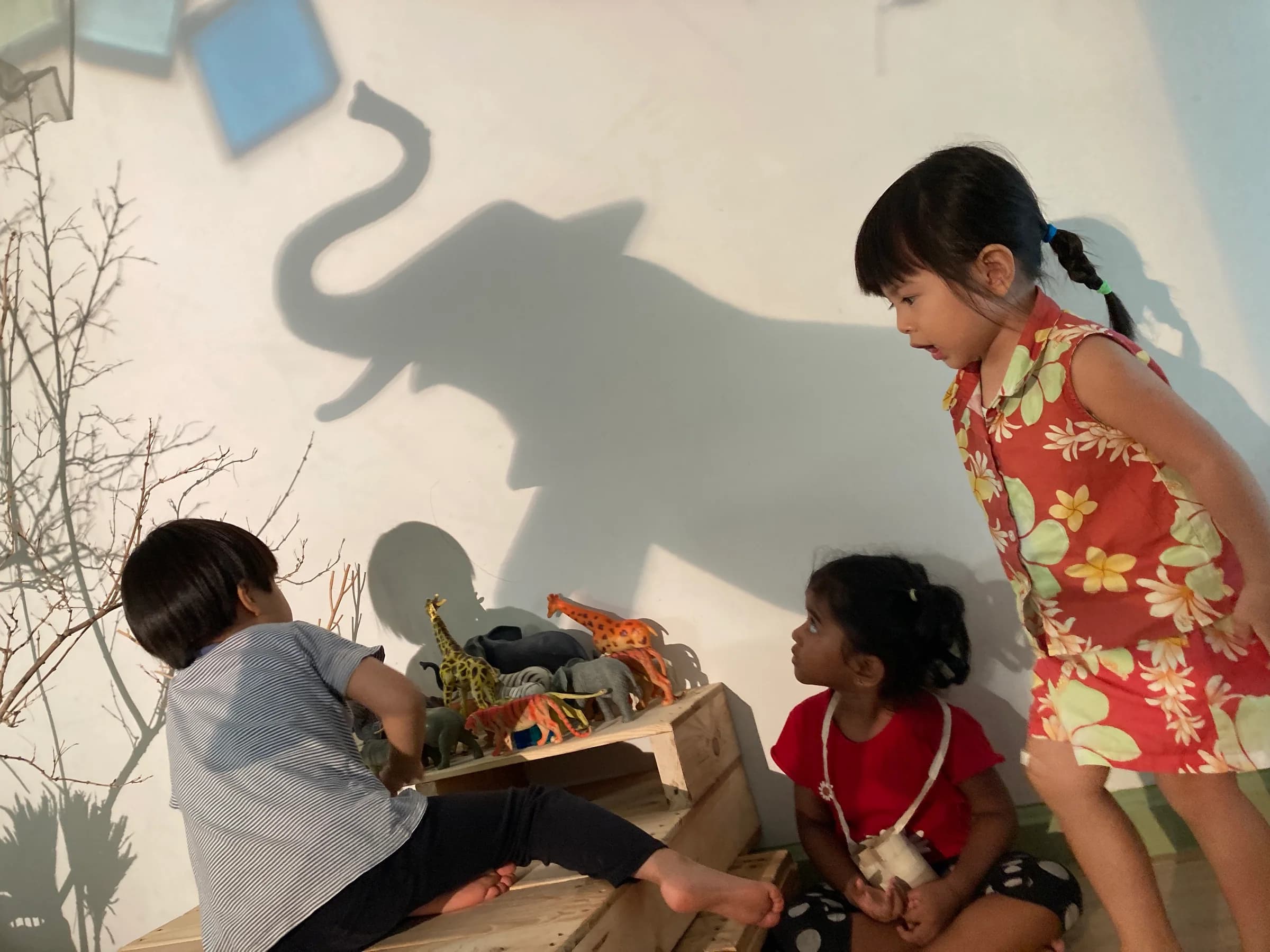 Three children exploring animal figures through light and shadow