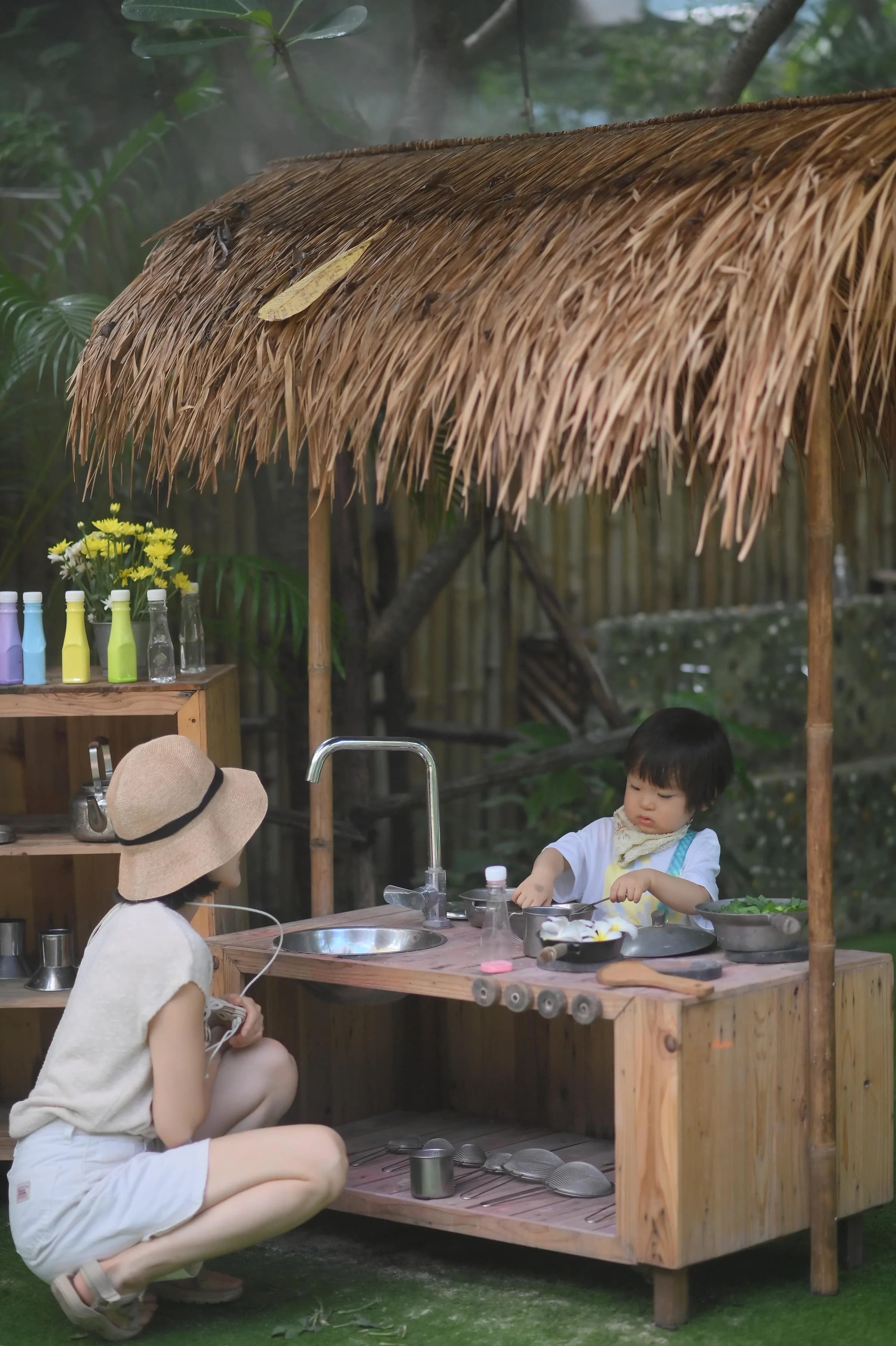 An educator joining a child at Annabel's outdoor play kitchen