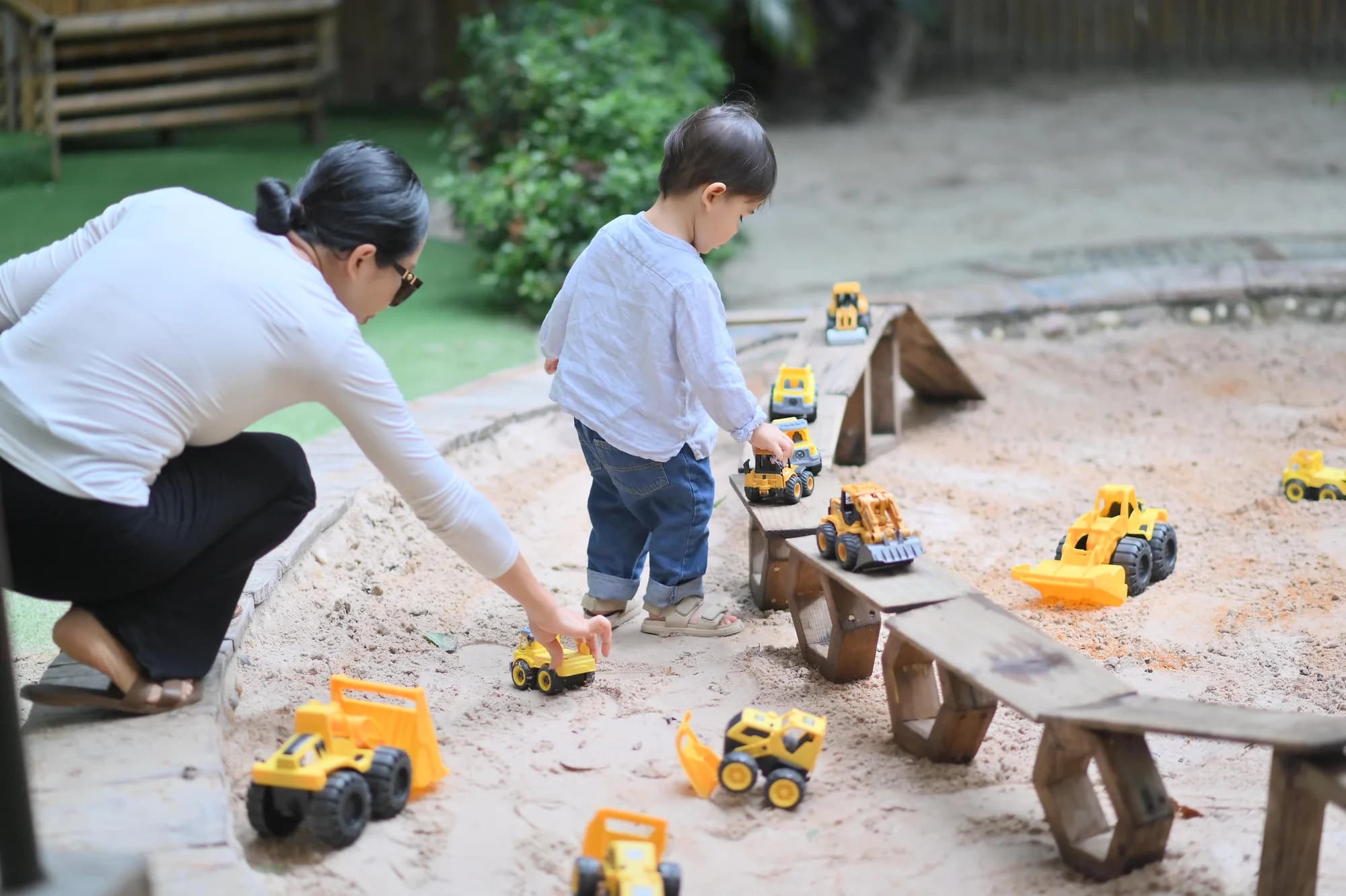 A child and grown-up playing with toy trucks in the sandpit